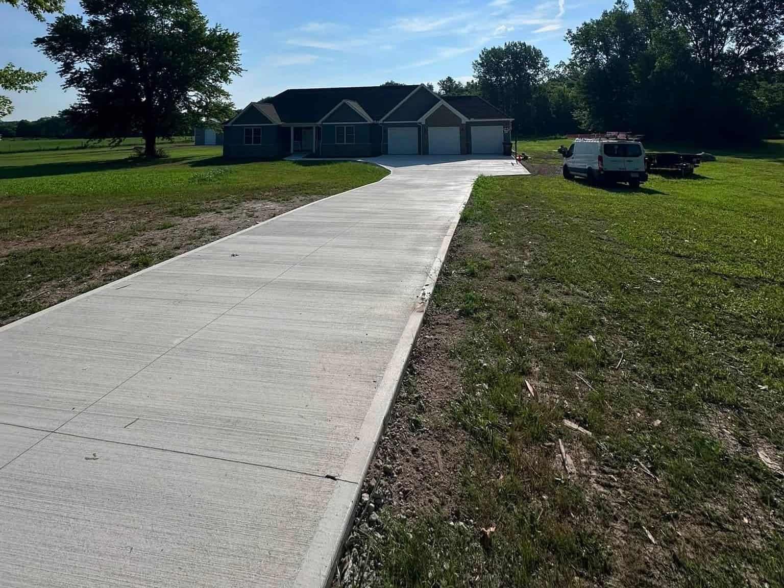 Long broom-finish concrete driveway leading to a three-car garage at a country ranch home