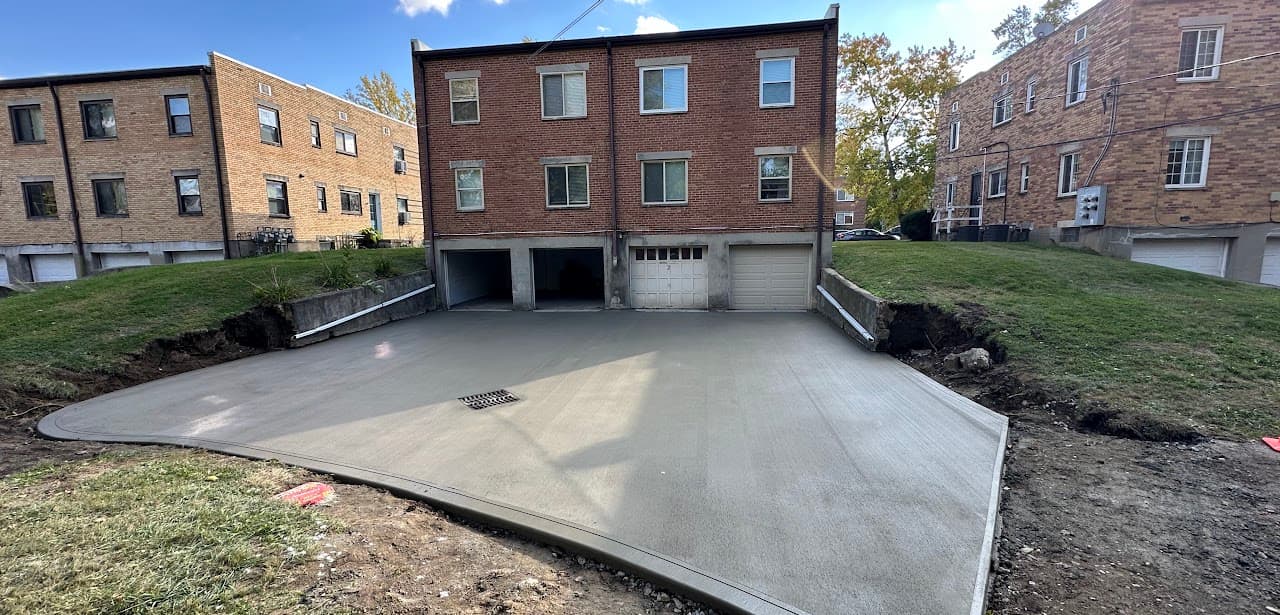 Wide concrete driveway and drainage in front of a 3-story brick apartment building