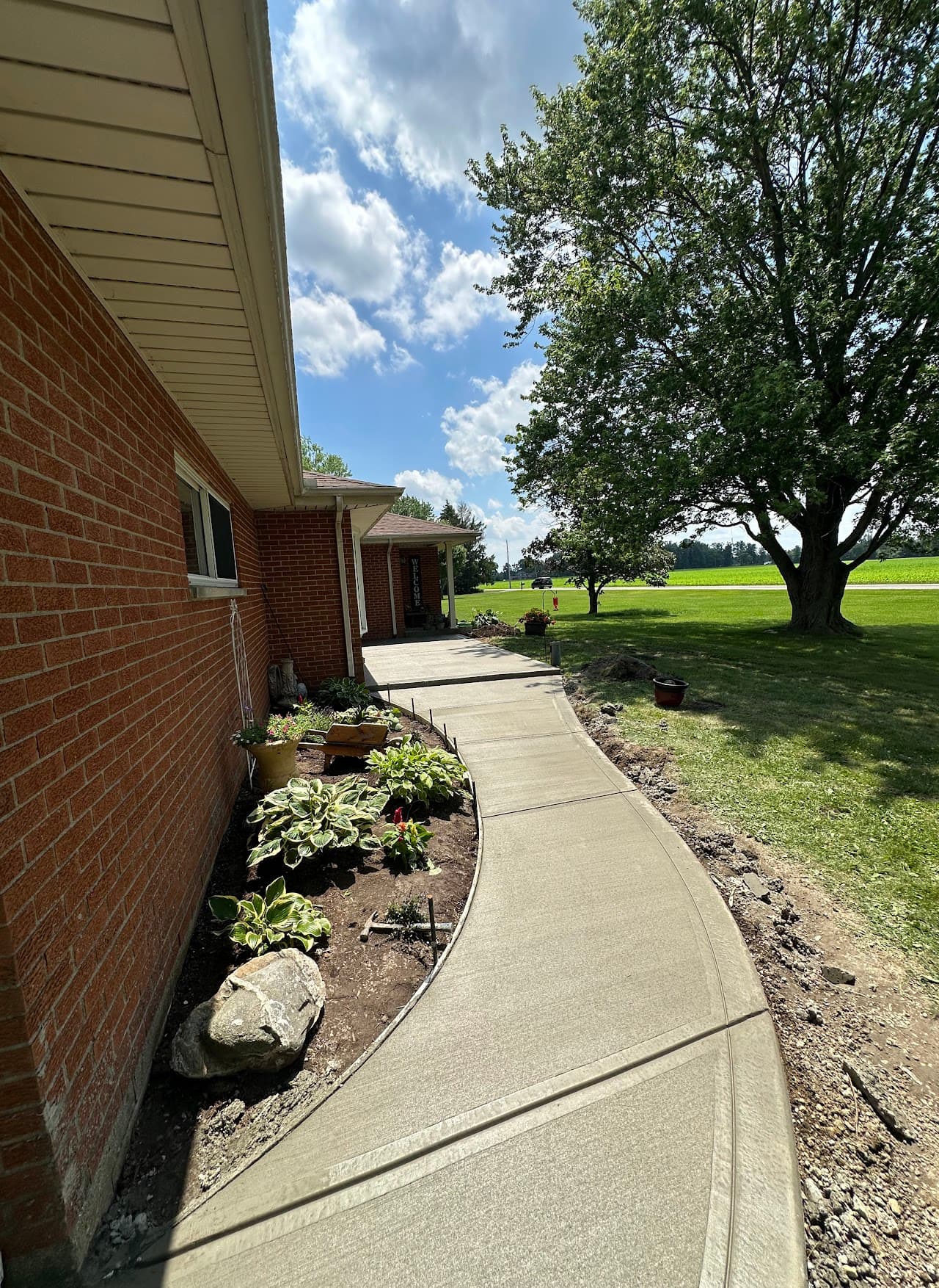 Long concrete sidewalk along a brick home with summer skies
