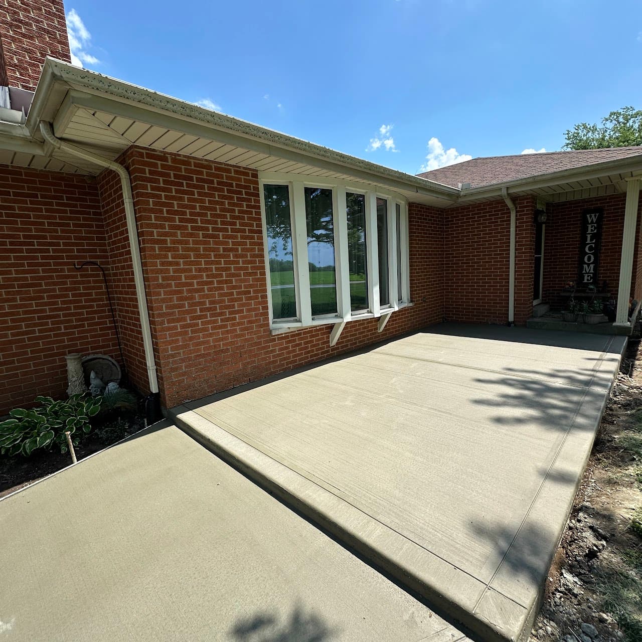 Covered brick porch entry with broom-finish concrete and welcome sign