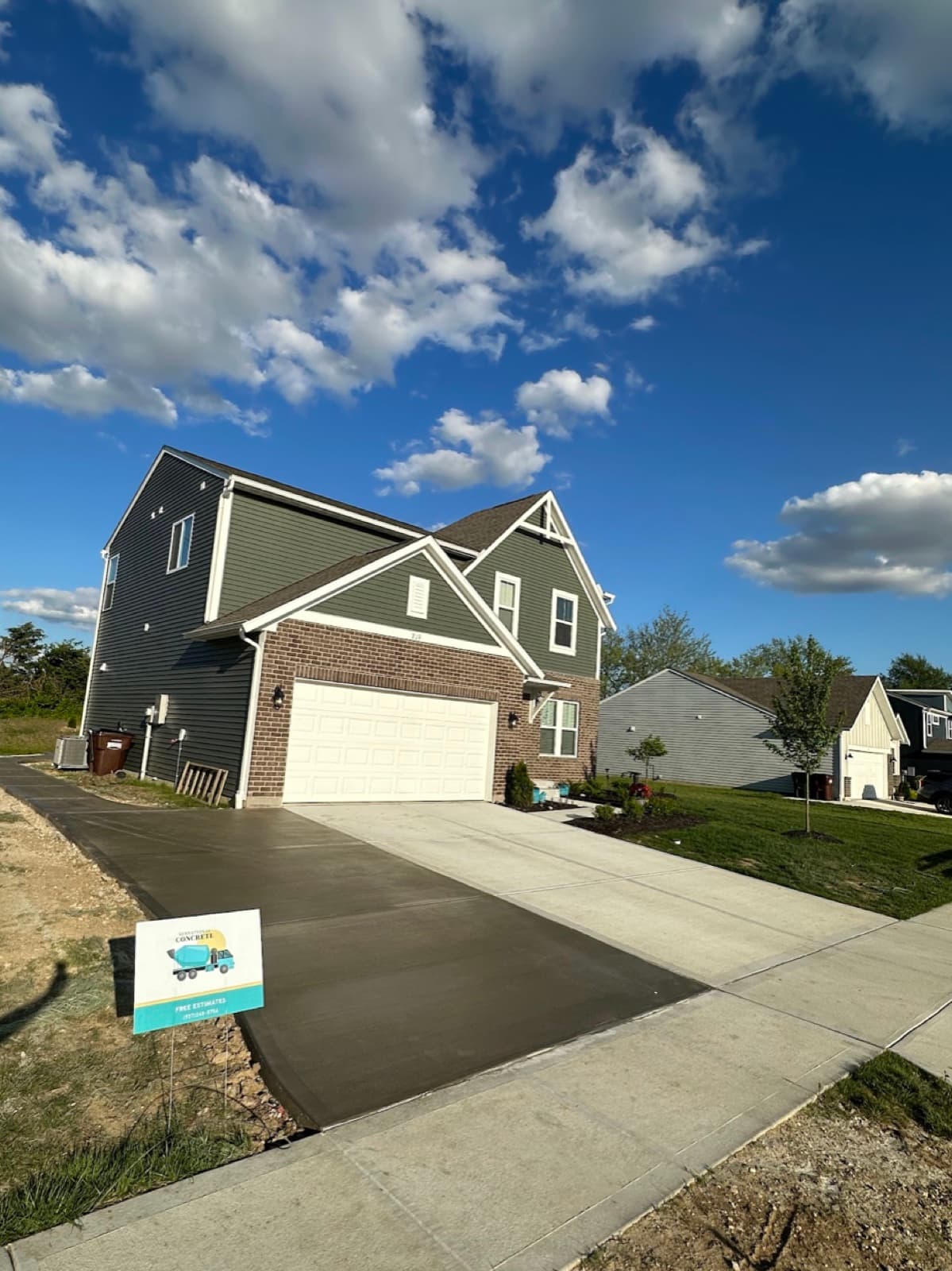 Fresh concrete driveway extension at a two-story home with Sensational Concrete yard sign