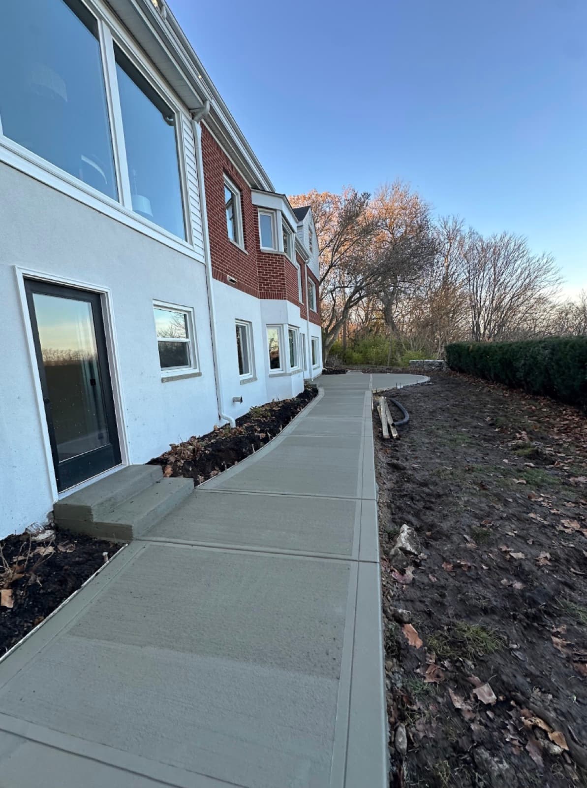 Curved concrete sidewalk alongside a stucco-and-brick building at golden hour