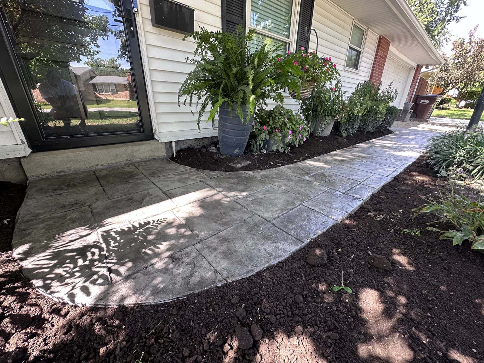 Stamped concrete front stoop and walkway curving past fresh landscaping